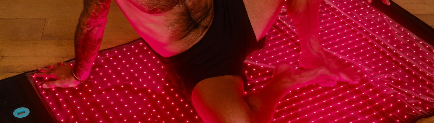 Man sitting on the oversized HigherDOSE LED light therapy mat on a wood floor