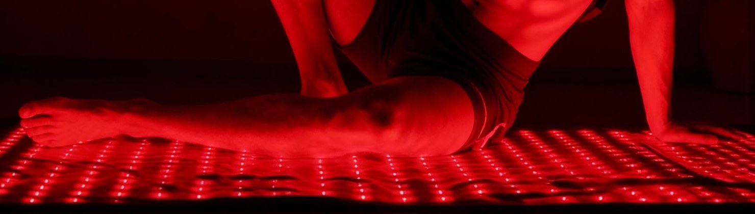 Man resting on the glowing Nuvio red light therapy mat in a dark room